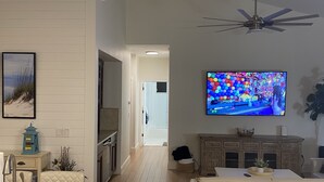Een moderne woonkamer met een flatscreen televisie, een plafondventilator en een keuken met een eettafel en stoelen.