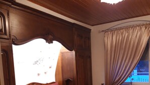 Ein Schlafzimmer mit einem hölzernen Bett, einem Fenster mit Vorhängen und einer Heizung.