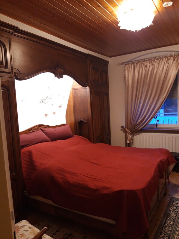 A bedroom with a wooden bed, a window with curtains, and a radiator.
