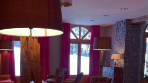 A spacious living room with a stone wall, leather armchairs, a wooden coffee table, and a large window with curtains.