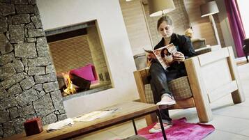 A person sitting on a wooden chair reading a magazine in a room with a stone wall, a fireplace, and a pink rug.