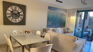 A modern living room with a dining area, featuring a large wall clock, a sofa set, and a painting of a wave. - Luxury apartment with lovely views over Marina (Marina de Sotogrande, San Roque)