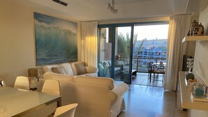 A modern living room with a large sofa, a dining table with chairs, and a view of the outside balcony. - Luxury apartment with lovely views over Marina (Marina de Sotogrande, San Roque)