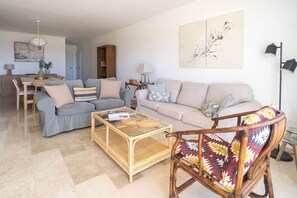 A living room with a sofa, a coffee table, and a chair. There is a dining area with a table and chairs.