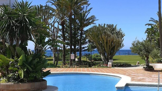 Una piscina con vista sull'oceano, circondata da palme e un edificio bianco.