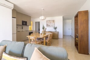 A modern kitchen with built-in appliances, a dining area with a wooden table and chairs, and a hallway leading to a bedroom.