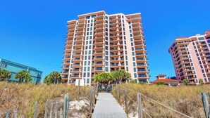 A high-rise hotel with multiple balconies, a pathway leading to the entrance, and a clear blue sky. - SeaChase 1005C by Liquid Life (Orange Beach)