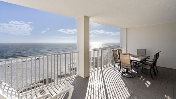 A balcony with a view of the ocean, a table with chairs, and a white chair. - Pelican Pointe 702 by Liquid Life (Orange Beach)