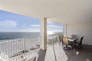A balcony with a view of the ocean, a table with chairs, and a white chair. - Pelican Pointe 702 by Liquid Life (Orange Beach)