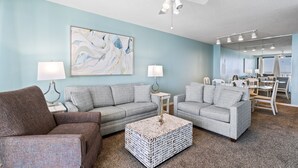 A living room with two grey sofas, a coffee table, and a ceiling fan. - Pelican Pointe 702 by Liquid Life (Orange Beach)