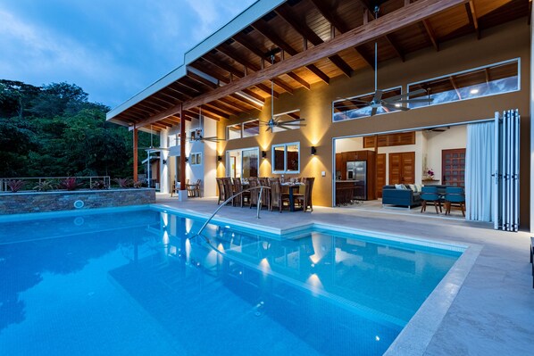 Une maison moderne dotée d’une piscine, d’un espace repas extérieur et d’un patio couvert.