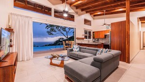 A modern living room with a grey sectional sofa, a glass coffee table, and a view of the ocean through large windows. - Luxury retreat with panoramic ocean view, private infinity pool, concierge (Uvita)