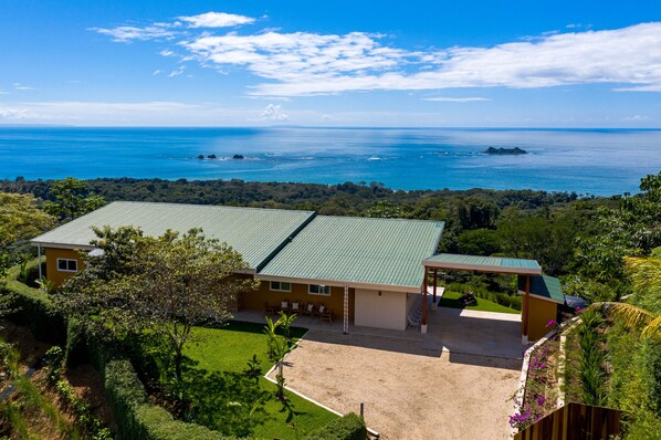 A two-story house with a green roof, a covered patio, and a view of the ocean.