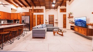 A modern kitchen with wooden cabinets, a stainless steel refrigerator, and a bar area with stools. - Luxury retreat with panoramic ocean view, private infinity pool, concierge (Uvita)
