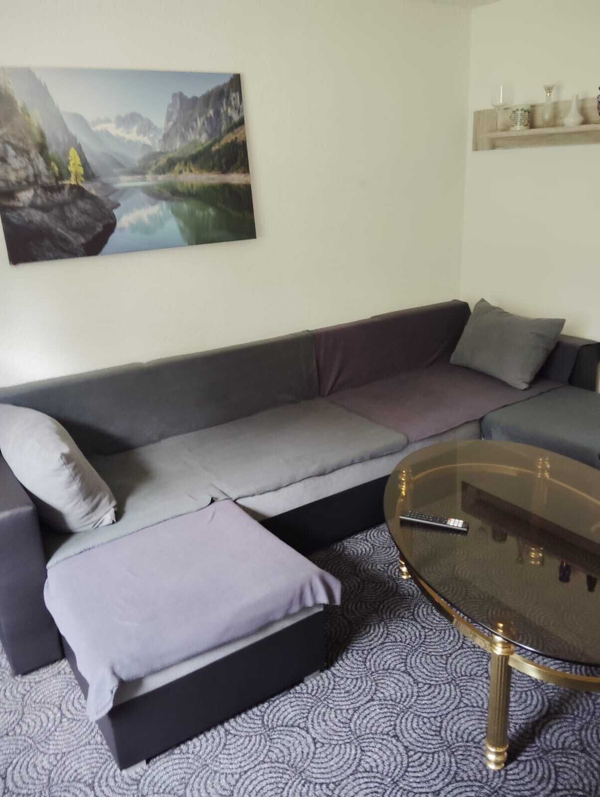 A modern living room with a grey sofa, a glass coffee table, and a painting of a mountain landscape on the wall.
