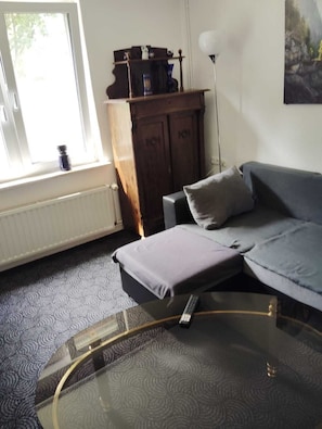 Ein Wohnzimmer mit einer Couch, einem Glastisch, einem Schrank und einem Bild an der Wand.