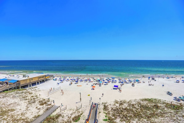 Relax on the beach with lounge chairs and umbrellas, steps from a scenic ocean view and a nearby building with a flat roof.