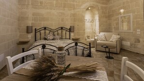 Un dormitorio con pared de piedra, una cama con ropa de cama floral, una mesita de noche con lámpara y una pequeña mesa con una botella y cañas.
