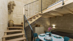 Comedor con una mesa redonda preparada para cuatro, escaleras de madera y una pared de piedra.
