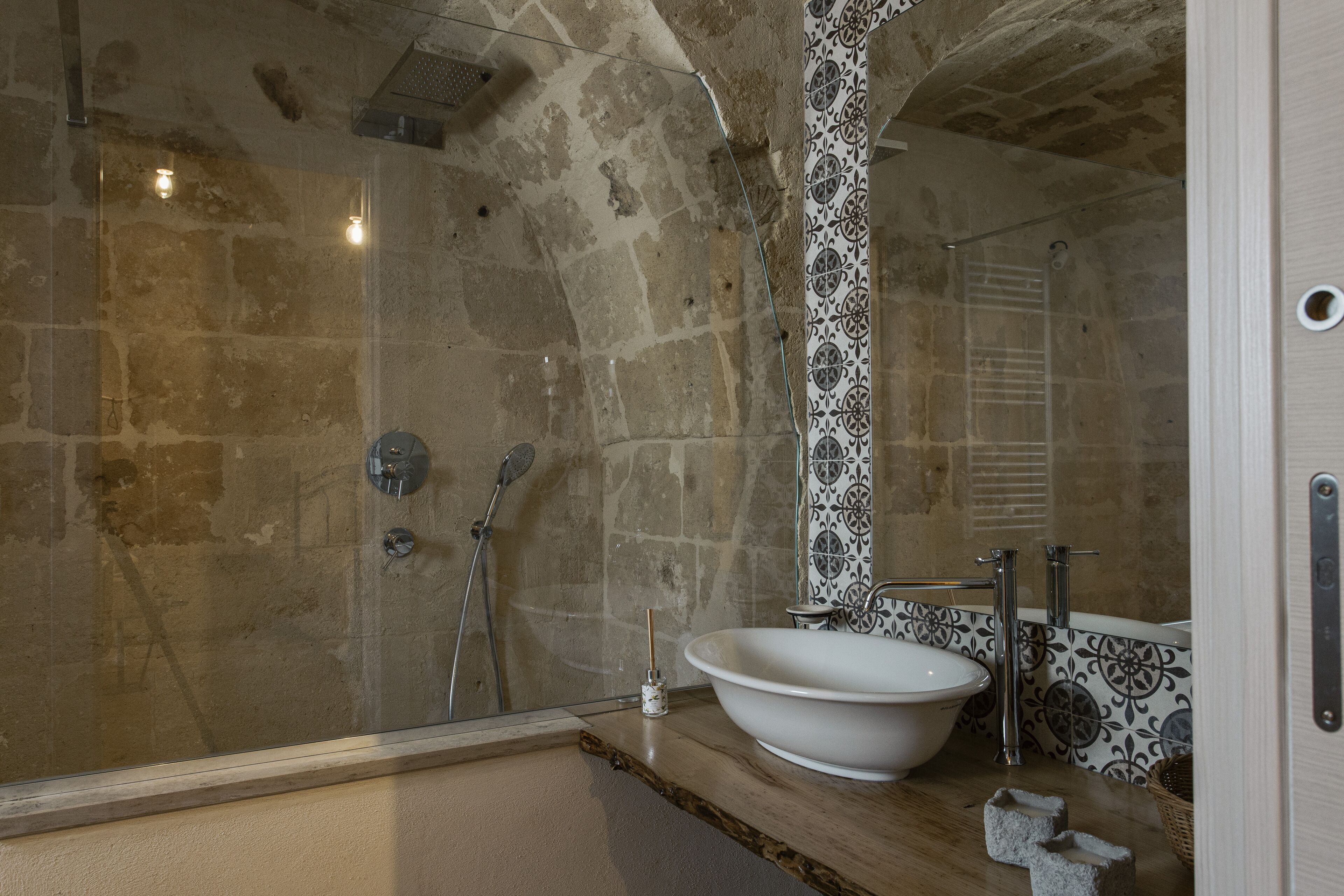 Ein Badezimmer mit einer Steinwand, einem weißen Waschbecken, einer Dusche und einer gefliesten Rückwand.