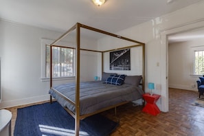Una cama con dosel, con una colcha gris, dos almohadas azules y una mesita de noche roja con una lámpara.