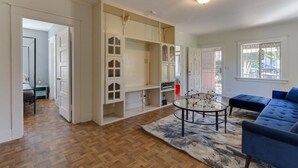 Een ruime woonkamer met een blauwe bank, een glazen salontafel en een ingebouwde witte boekenkast.