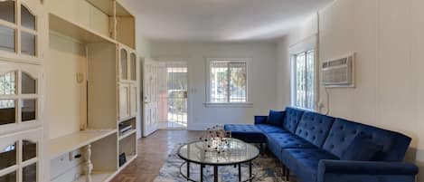A spacious living room with a blue sofa, a glass coffee table, and built-in shelving.