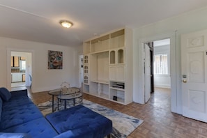 Una sala de estar con un sofá azul, una mesa de centro de vidrio y un mueble de entretenimiento blanco.
