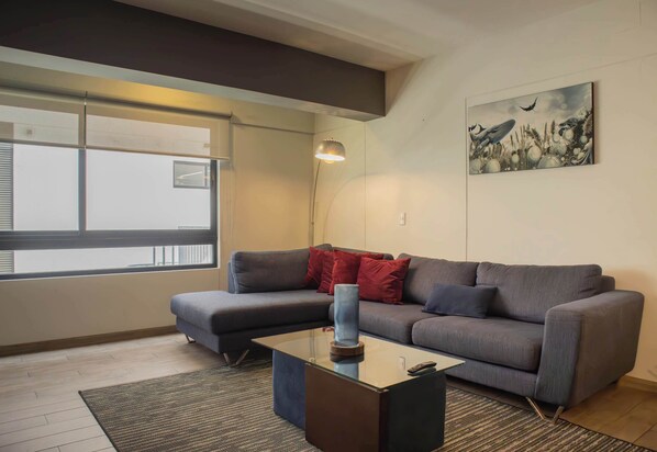 Een moderne woonkamer met een grijze bank, een glazen salontafel en een schilderij aan de muur.