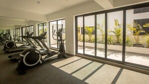 A gym with exercise equipment and large windows overlooking a courtyard with plants.