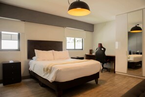Een moderne slaapkamer met een groot bed, een bureau en een stoel. Er is een garderobe met spiegel en een hanglamp.