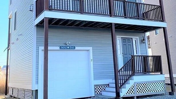 A two-story building with a garage door labeled "MAI TAI" and a balcony with a wooden railing. - 3-bd/3-bth, short walk to Salisbury beach and center - Winter Rentals Available (Salisbury)