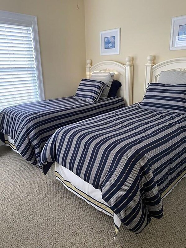 A bedroom with two single beds, beige walls, and a window with blinds. - 3-bd/3-bth, short walk to Salisbury beach and center - Winter Rentals Available (Salisbury)