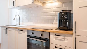 A modern kitchen with white cabinets, a stainless steel oven, a coffee machine, and a wooden countertop.