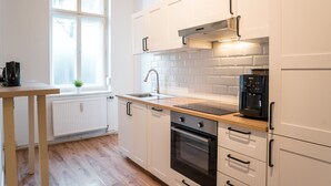A modern kitchen with white cabinets, a stainless steel range hood, a built-in oven, and a coffee maker on the countertop.