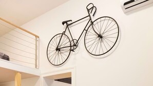 Een moderne hotelkamer met een eettafel gedekt voor vier personen, een fiets aan de muur en een vaas met gele bloemen op de tafel.