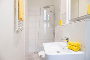 Moderni kylpyhuone, jossa on valkoinen pesuallas, keltaiset pyyhkeet, suihku ja wc.