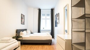 A compact bedroom with a bed, bedside tables, a dresser, and a window with curtains. - Great Apartment in Berlin Neukölln (Berlin)