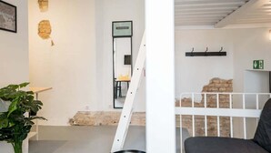Een kamer met een witte muur, een kleine tafel, een stoel, een plant en een trap naar een ander niveau.
