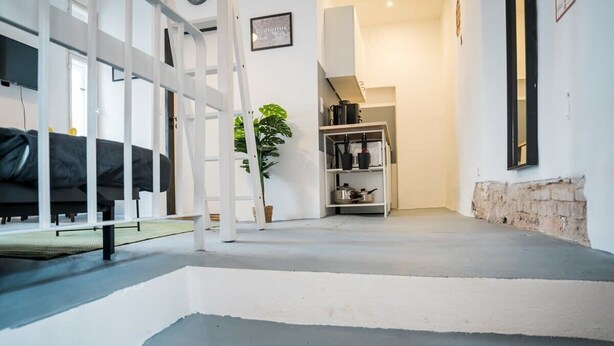 Een modern interieur met een trap naar een vide, een bed, een plant en een keuken met kasten.