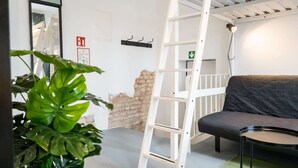 Een kamer met een grijze bank, een witte ladder, een groene plant en een bakstenen muur.