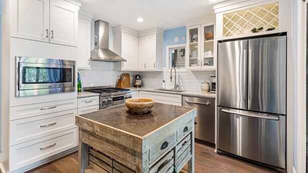 A modern kitchen with white cabinetry, stainless steel appliances, and a wooden island.