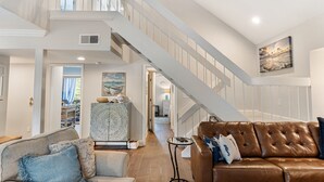 A spacious living area with a high staircase, a brown leather sofa, and a patterned cabinet.