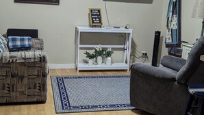 Un salon avec un téléviseur fixé au mur, une console blanche agrémentée d’objets décoratifs, un tapis à motifs et deux canapés.
