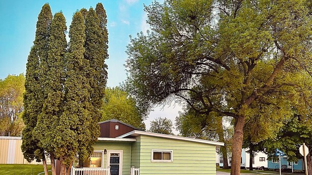 Une maison de plain-pied à l’extérieur vert, dotée d’un porche et d’une allée.