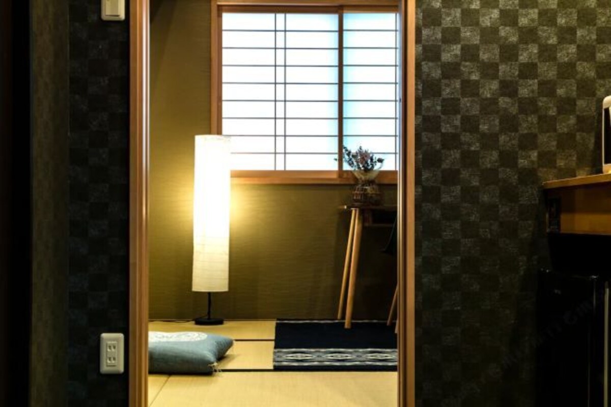 A traditional Japanese room with tatami flooring, a shoji screen, a low table with a vase, and a black cabinet.
