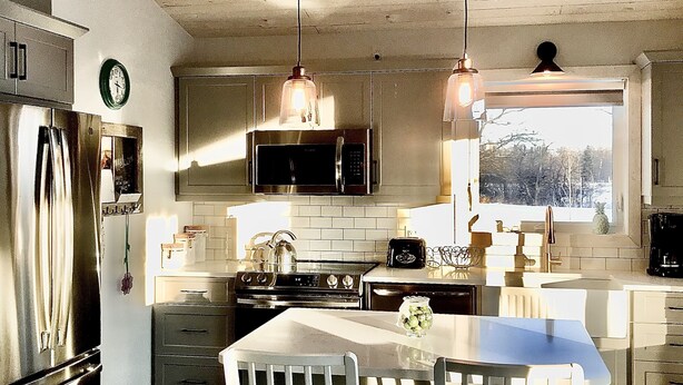Une cuisine avec un plafond en bois, des appareils électroménagers en acier inoxydable, une table à manger avec des chaises et une fenêtre donnant sur les arbres.