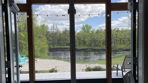 Une pièce dotée d’une grande porte-fenêtre coulissante donnant sur une terrasse extérieure d’où l’on peut admirer une rivière et des arbres.