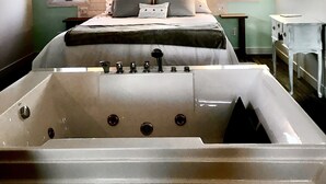 Une chambre avec une grande baignoire, un lit avec des oreillers, deux lampes fixées au mur et une fenêtre.