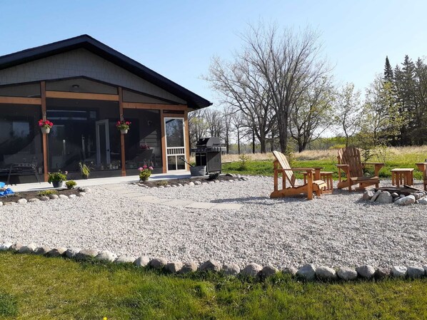En bygning med en overdækket terrasse, udendørs møbler inklusive Adirondack-stole, og en grill.